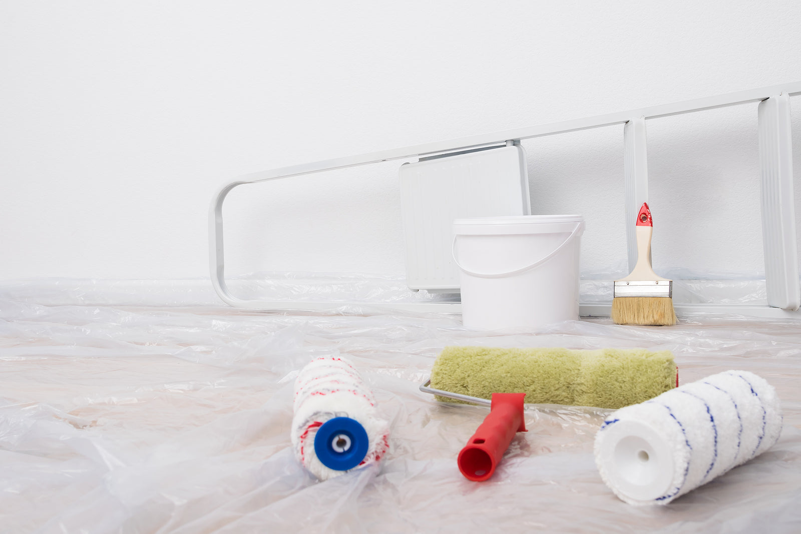 Indoor wall painting equipment and stairs|Rear view of a male painter drawing a wall with paint roller and a separate tank from a large empty space with wooden stairs.