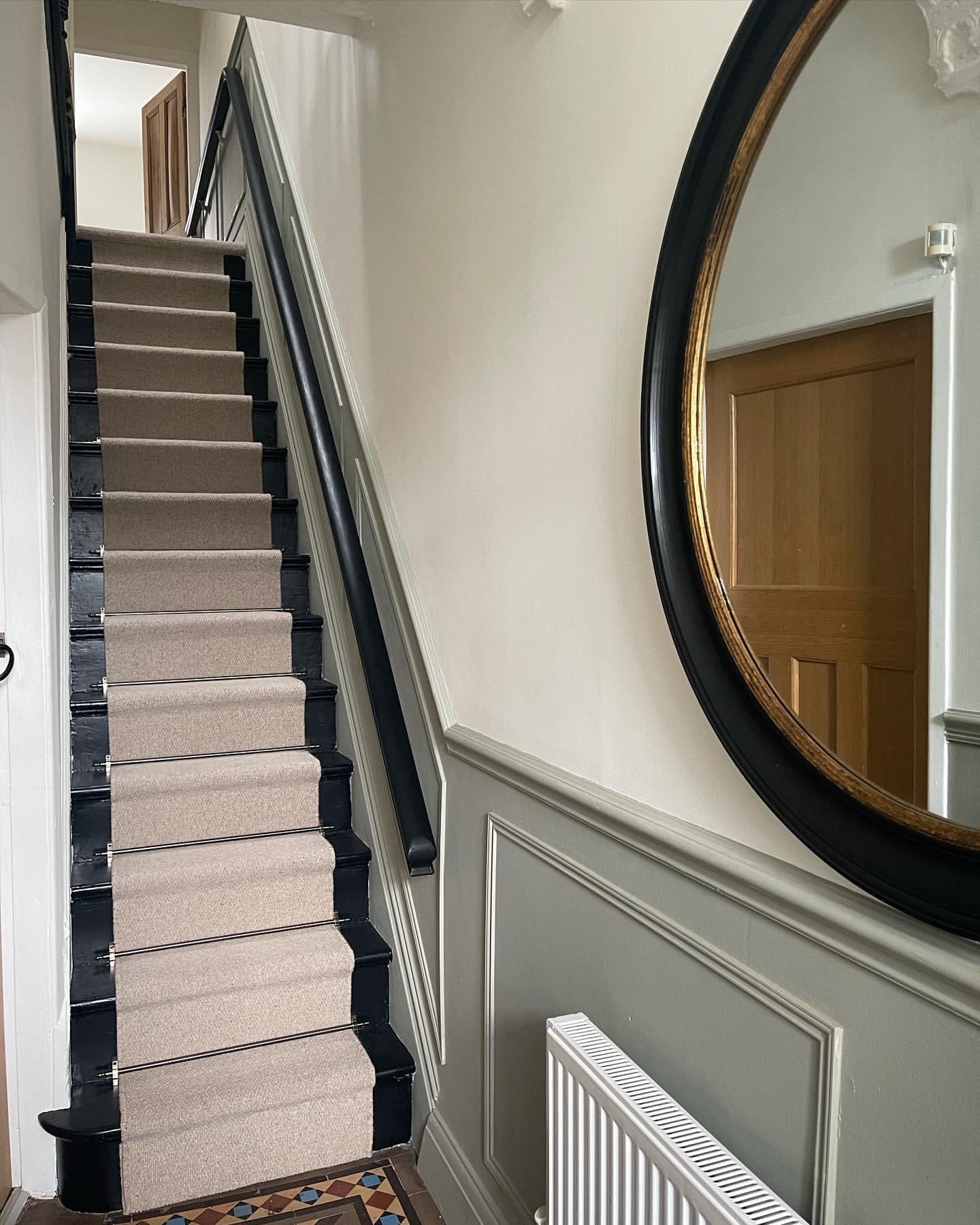 Modern hallway with beige carpet runner and black stair rods. The walls have sage green wainscotting.