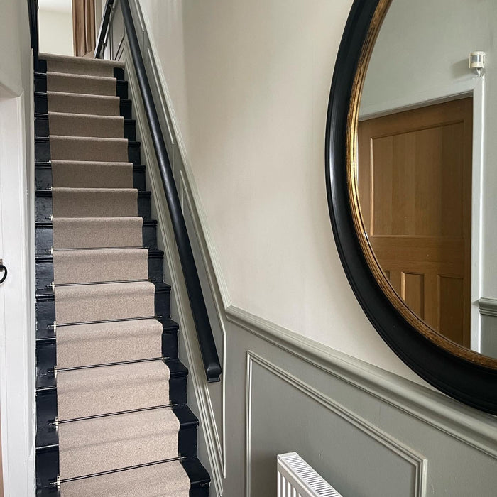 Modern hallway with beige carpet runner and black stair rods. The walls have sage green wainscotting.